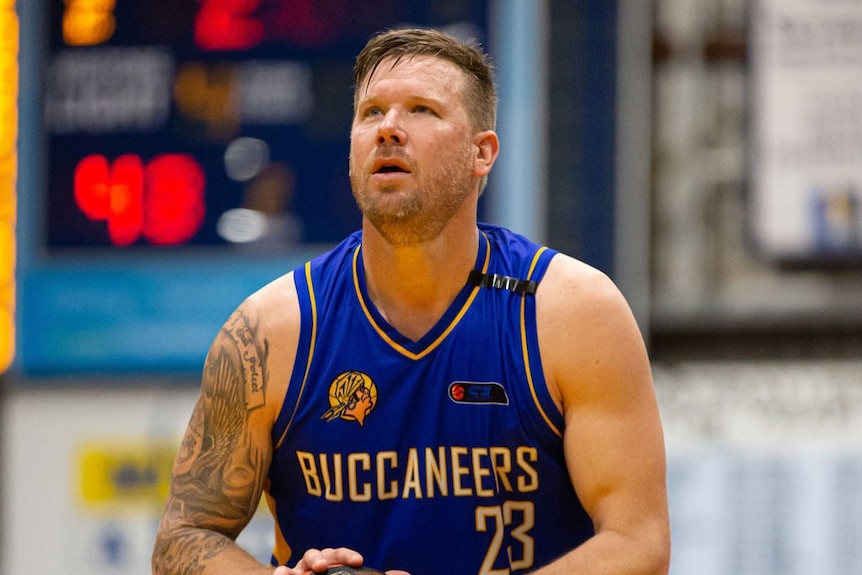 A man wearing a blue basketball uniform looks up as he holds a basketball