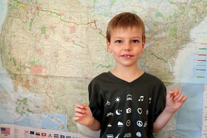 A young boy stands in front of a map of America with a route drawn across it in coloured pen