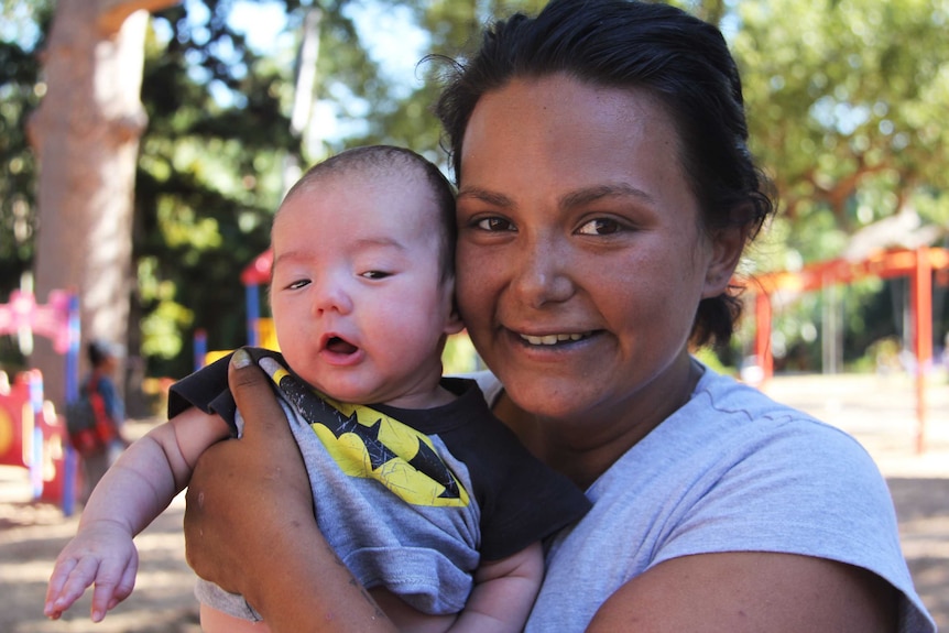 A woman holds her newborn son in a park.