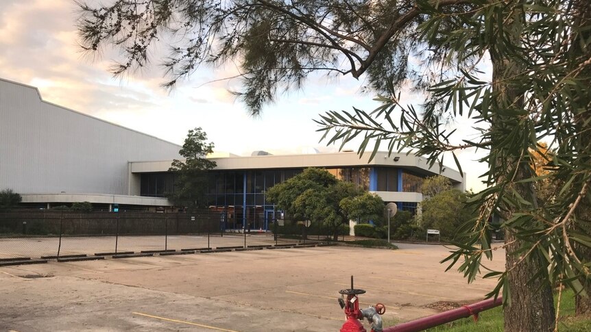 A building with a carpark and a tree in the foreground.