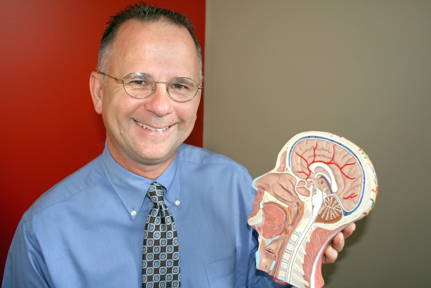Man standing with a cross-section model of a brain and head.