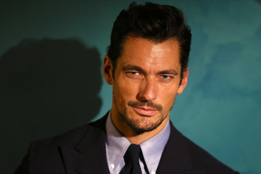 A man with black hair, neat stubble and a square facial bone structure wearing a suit.