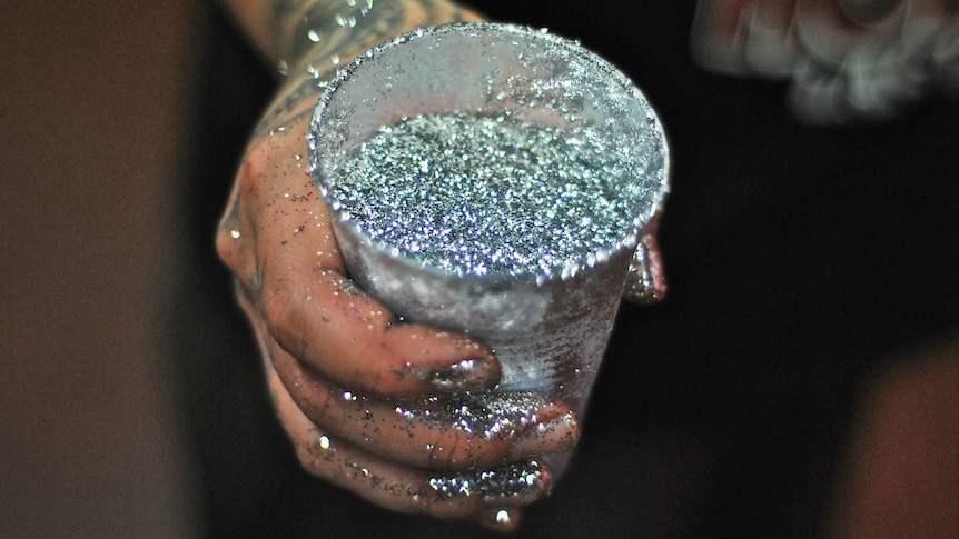 A woman holds a cup full of silver glitter.