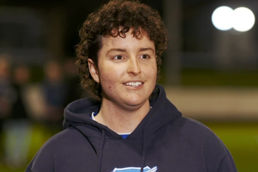 Woman wearing a navy hoodie on a football field.