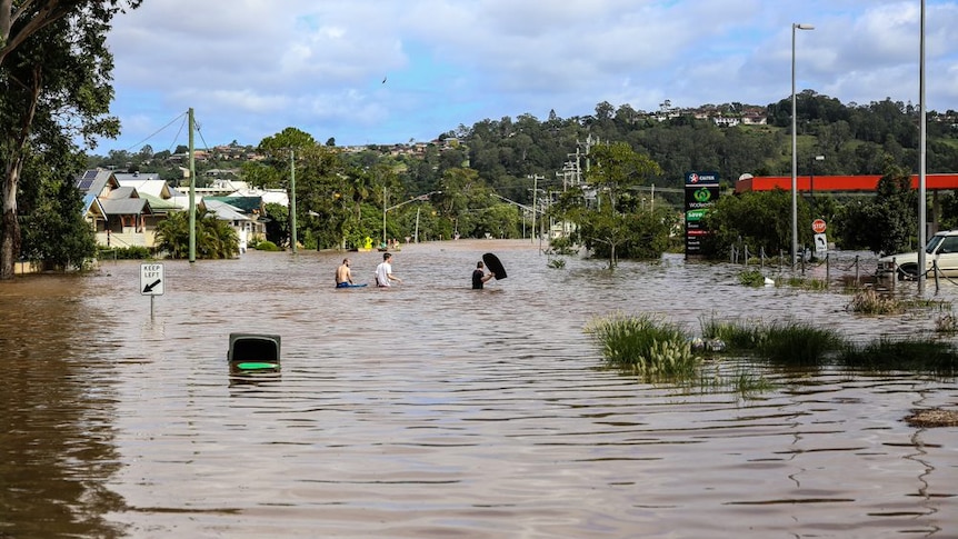 Boys walking through floodwater in Lismore, near a totally inundated service station.