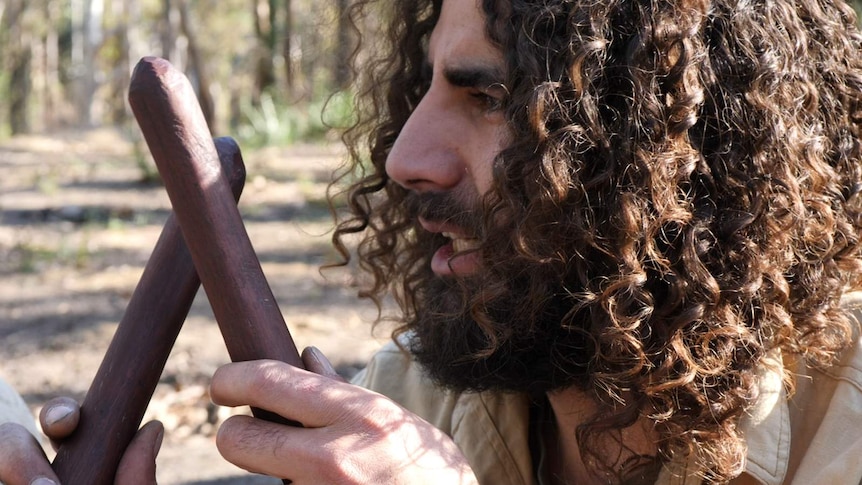 Indigenous man holding clapsticks about to speak