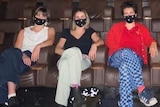 People sit in theatre seats, wearing masks.