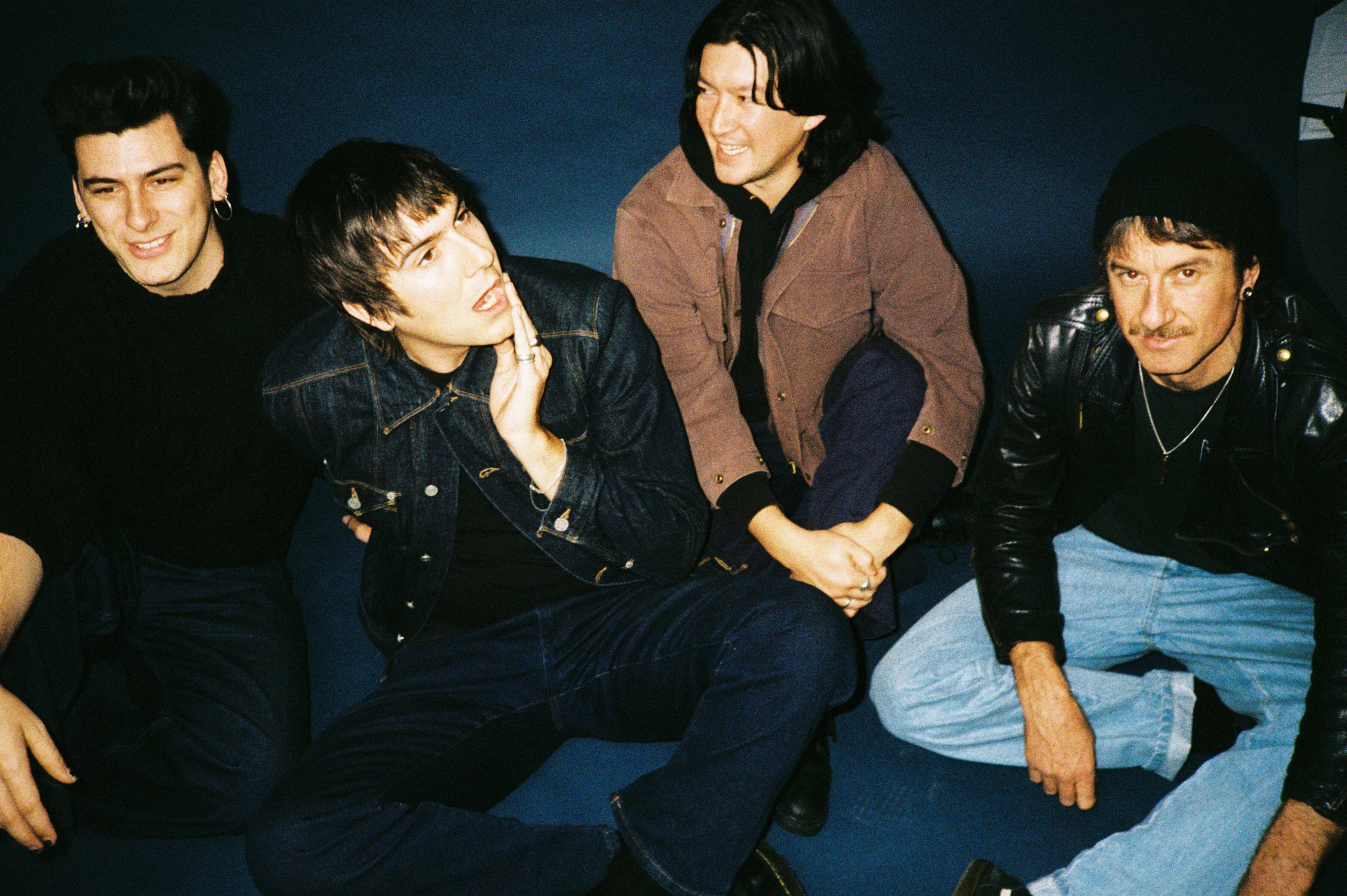 Four men sitting on ground in a band publicity photo