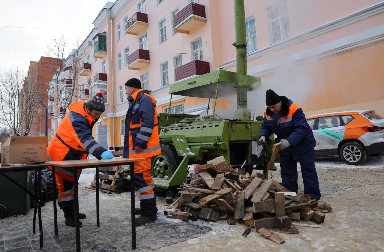 Three men in uniform working near a large machine with smoke coming out of it. A pile of wood can be seen nearby, too.