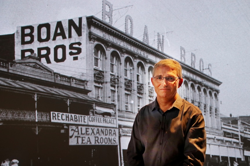 A man stands in front of a giant screen displaying an large black and white image