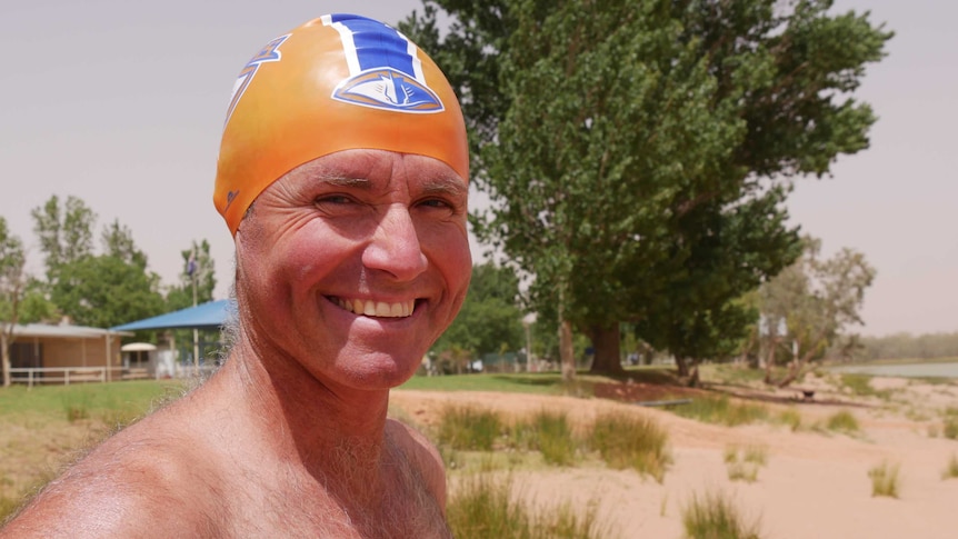 Brendan stands one the shore of Lake Copi, wearing a Broken Hill Stingrays swim-club swimming cap.