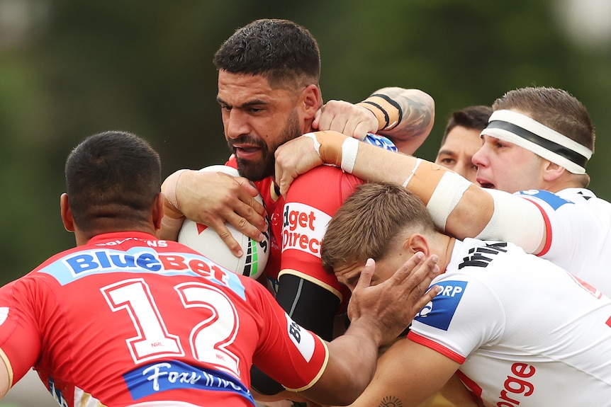 A Dolphins NRL player holds the ball as he is tackled by St George Illawarra opponents.