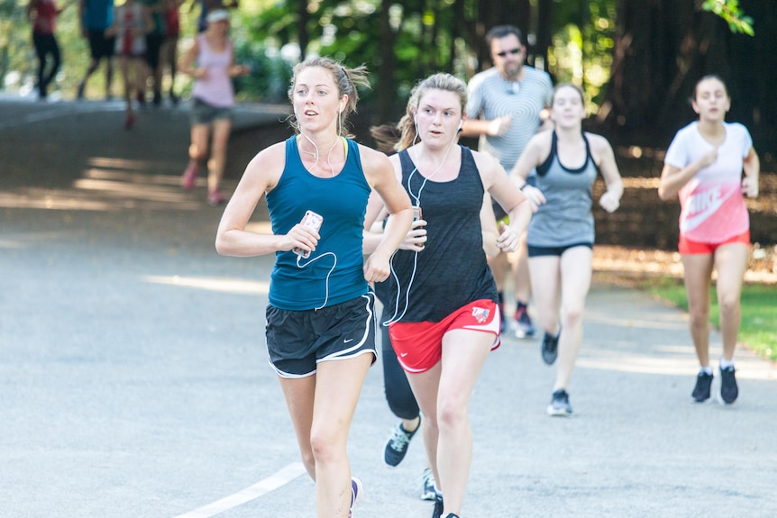Two women at parkrun run with headphones and a mobile phone.