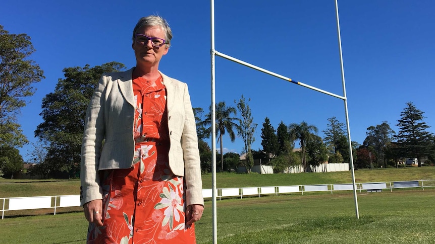 .A woman stands on a sporting field in front of the football goal and stands.