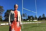 .A woman stands on a sporting field in front of the football goal and stands.