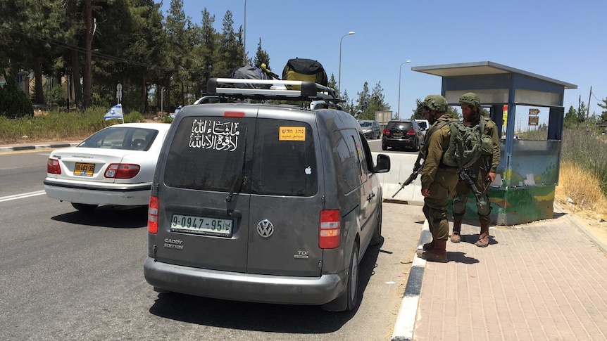 Two soldiers stop a Palestinian's car at a checkpoint near Gush Etzion, while an Israeli car drives past.