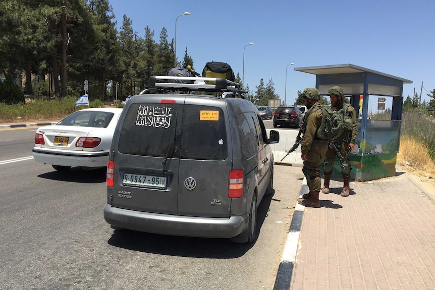 Two soldiers stop a Palestinian's car at a checkpoint near Gush Etzion, while an Israeli car drives past.