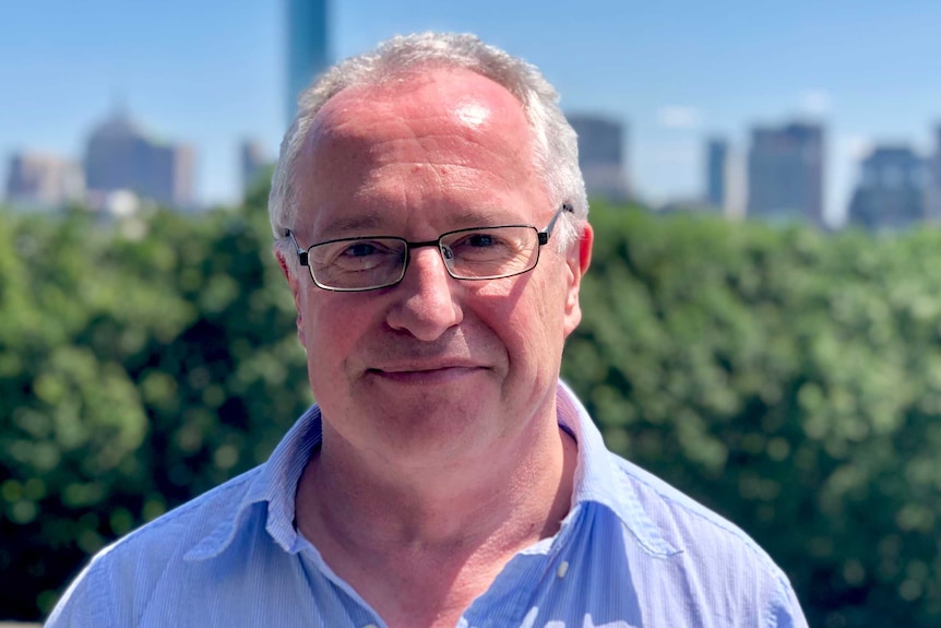 A man standing in the sunshine in front of a city and parkland backdrop.