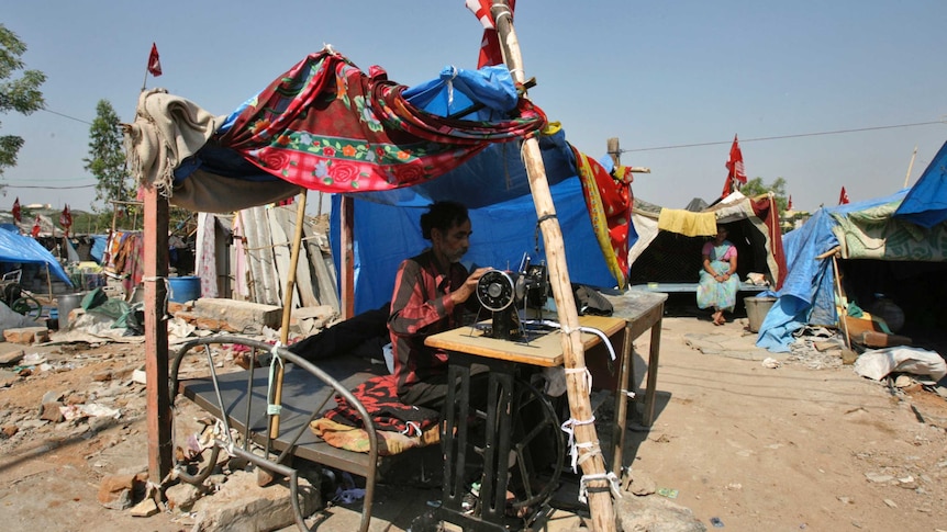 A man sewing with a sewing machine under a makeshift tailoring shop made my tarpaulin and fabric.