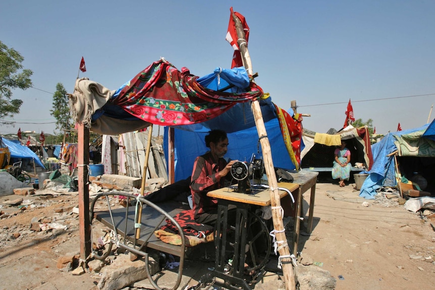 A man sewing with a sewing machine under a makeshift tailoring shop made my tarpaulin and fabric.