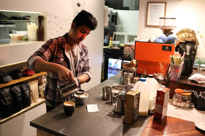 A staff member pours milk from a jug into a cup.