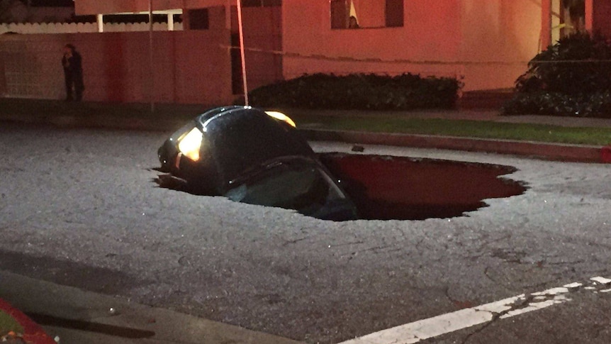 The bonnet of a car sticks out from the pavement on a California road, after falling in a sinkhole.