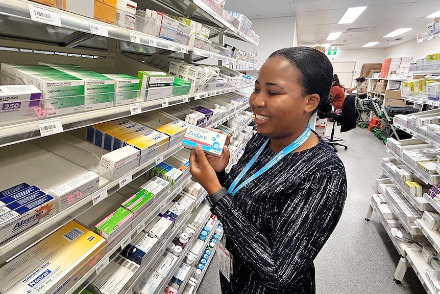 Female pharmacist standing between rows of medications in a pharmacy.