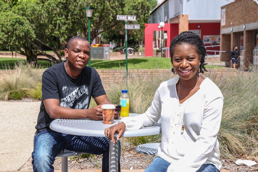 An African man and woman sit at a table outside at a university campus