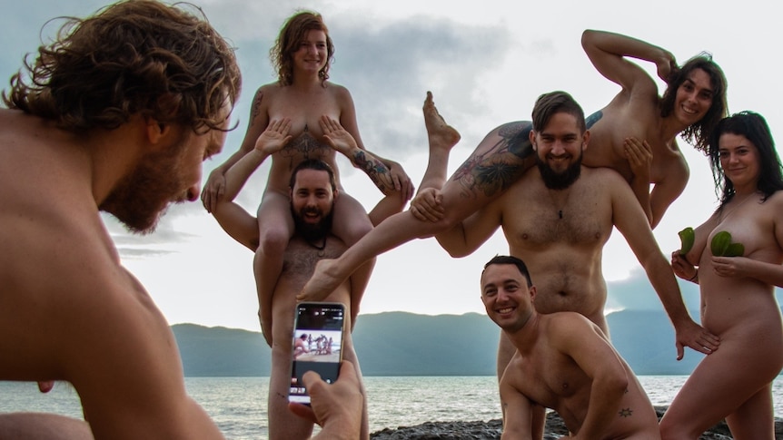 A group of people pose for a photo on a beach while naked 