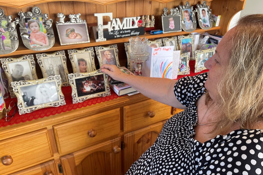 A woman in a black and white polka dot dress looking at framed family photos. 