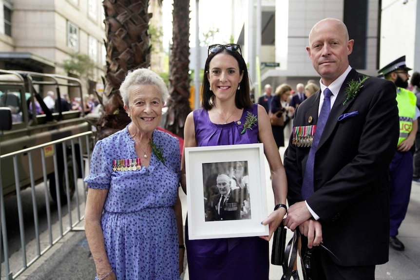 two women and a man holding a black and white portrait of veteran soldier