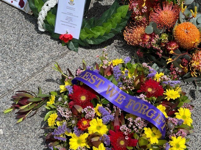 A floral wreath laid on the ground with a ribbon reading "lest we forget".