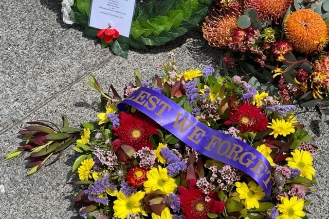A floral wreath laid on the ground with a ribbon reading "lest we forget".