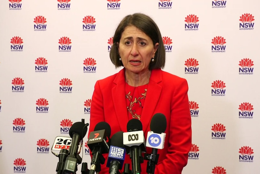 NSW Premier Gladys Berejiklian stands at a lectern with microphones pointed at her.