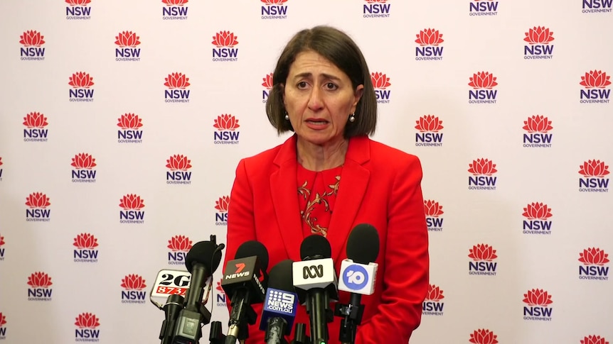 NSW Premier Gladys Berejiklian stands at a lectern with microphones pointed at her.