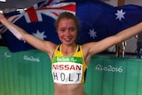 Isis Holt holds up the Australian flag as she smiles at the camera