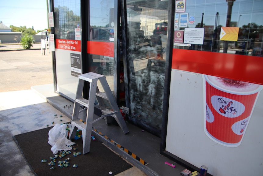 A building facade with a broken sliding door with a ladder and scattered lollies lying on the ground