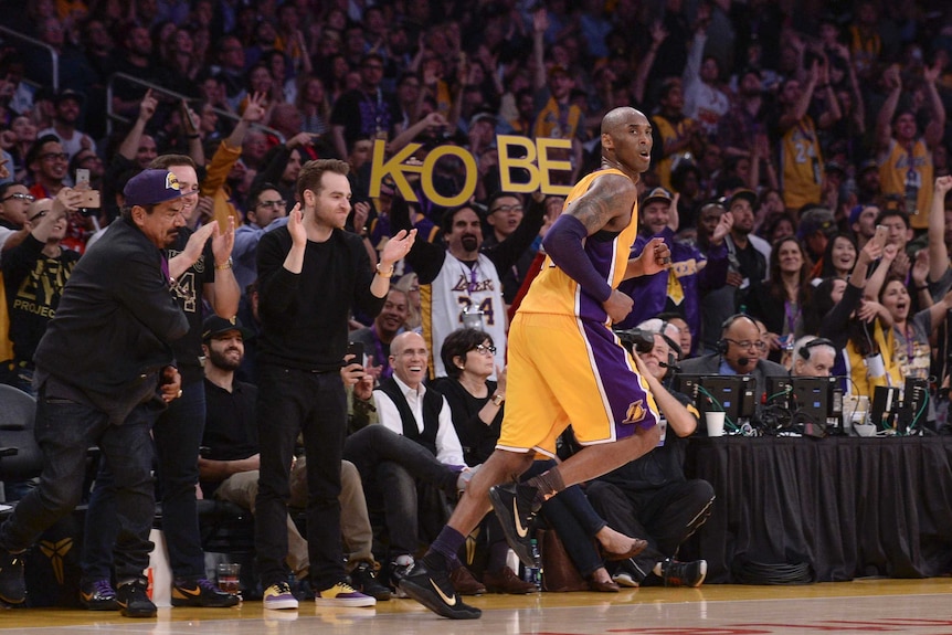 Kobe Bryant runs in front of supporters holding up a sign of his name