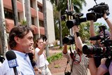 Matt Wright walks while surrounded by people holding cameras and microphones outside the Darwin Local Court.