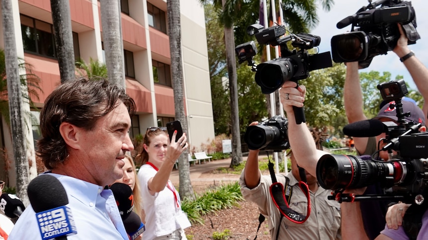 Matt Wright walks while surrounded by people holding cameras and microphones outside the Darwin Local Court.