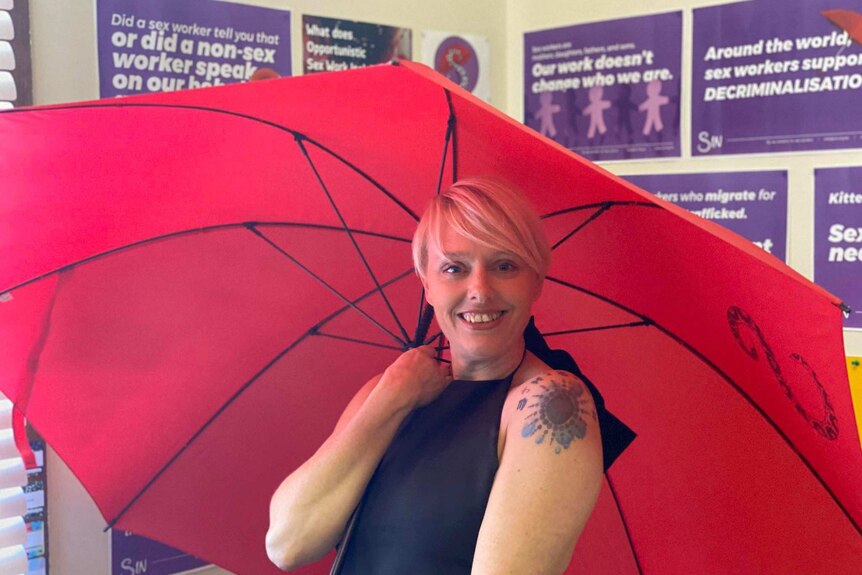 Sex Industry Network's Kat Morrison smiles as she holds an open red umbrella above her head.