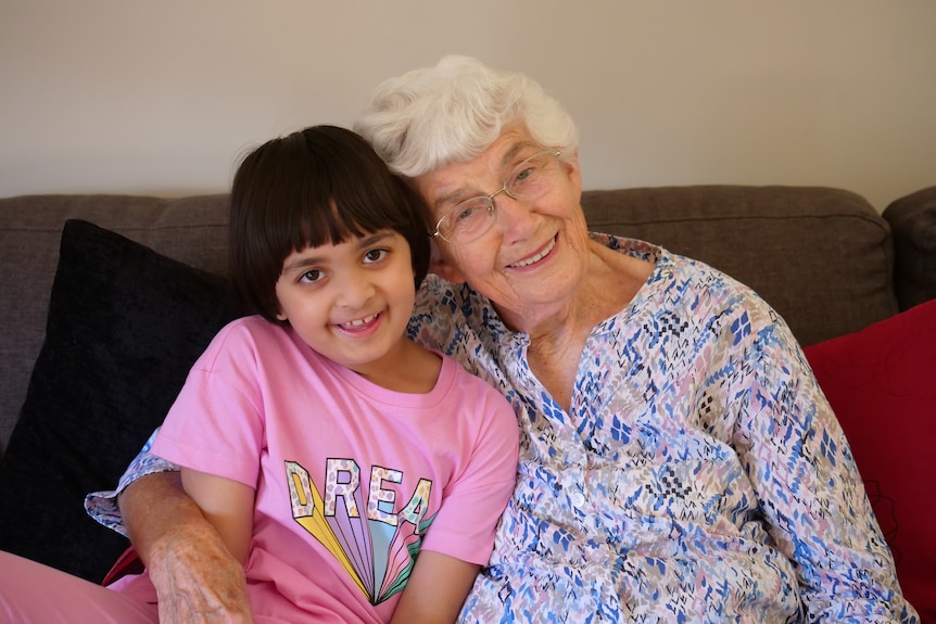 A young girl and an elderly woman on the couch, smile at the camera.