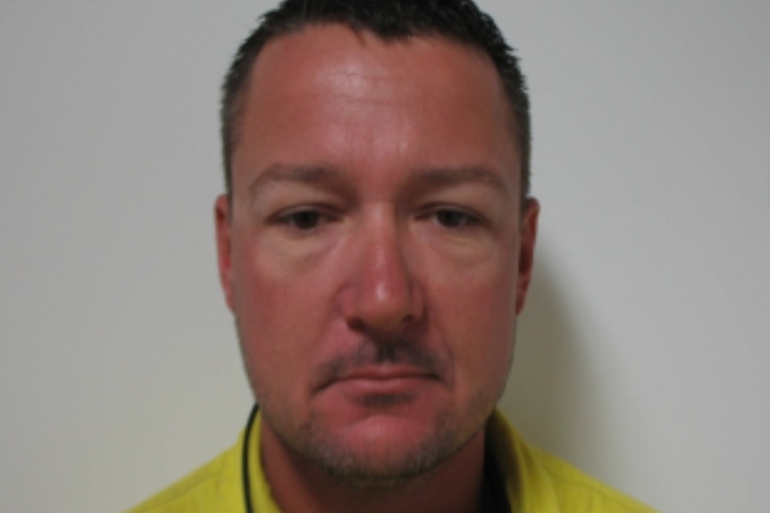 A mugshot of a man with dark hair, wearing a high visibility yellow shirt.