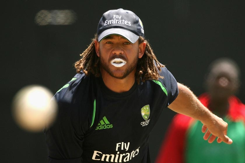 A cricketer wearing a cap – Andrew Symonds – bowls a ball.