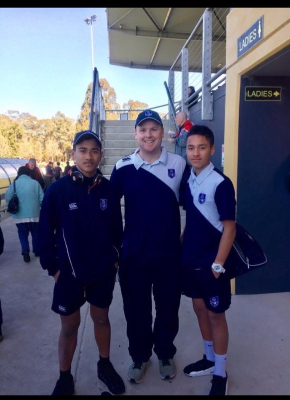 Dois meninos posam para uma foto com um treinador da liga de rugby 
