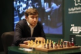 A man in a jacket looks at the camera in front of a chess board
