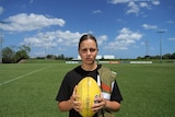 Danielle Ponter holds a football and sports an NT Thunder jersey slung over her shoulder in front of a lush playing field.