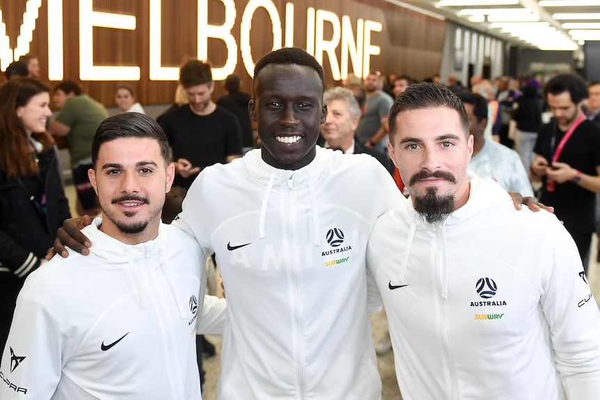 Three Socceroos squad members stand together at Melbourne Airport.