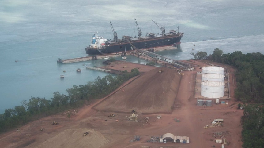 An aerial view of a 50-tonne ship at Port Melville, woodchip piles in foreground, August 2016