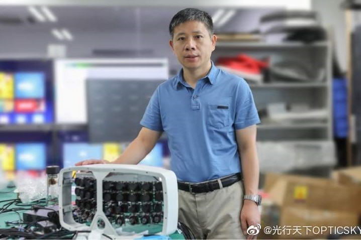 A man stands next to a large camera in an office setting.